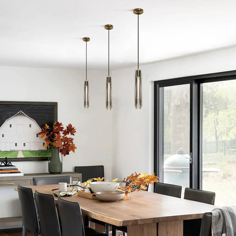 Dining room with Smokey Crystal Pendant Light In Antique Brass Gold Finish, long tube hanging fixture above wooden table.
