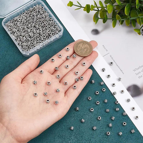 Close-up of hand holding antique silver tube spacer beads, 300 pcs, Tibetan zinc alloy, 4x5mm with 2.2mm hole. Ideal for DIY jewelry.