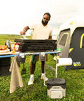 Man cooking on CORE FlexRail camp table with hanging organizer, featuring four zippered compartments and weather-resistant storage.