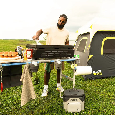 Man cooking on CORE FlexRail camp table with hanging organizer, featuring four zippered compartments and weather-resistant storage.