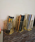 Gold Metal Two Pack Sticky Note Holder And Pen Holder Set with circle design on a desk holding pens and pencils.