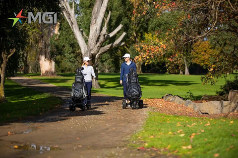 All Terrain Remote Controlled Electric Golf Caddy With Quick Zip Fold Setup Includes Drink Phone Umbrella Mounts Signature Power Bundle And Towel Keep It Smooth And Easy On The Daily, two users walking with golf caddies on a sunny path.