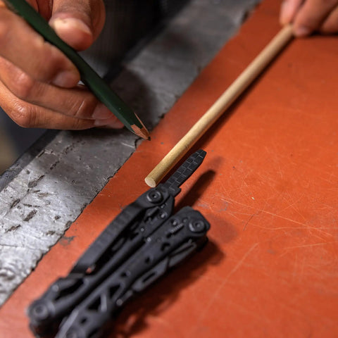 Open Suspension NXT 15 In 1 EDC Multitool With Needle Nose Pliers on workbench, next to wooden rod being marked with pencil.
