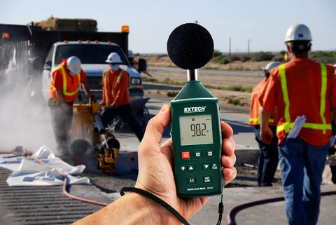 Compact Digital Sound Level Meter With Plus Minus 1dB Accuracy, Class 2, Backlit LCD used on job site with workers in background.