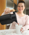 Woman pouring coffee from 50 Oz Stainless Steel Thermal Coffee Carafe Insulated Vacuum Double Walled Beverage Dispenser into mug.