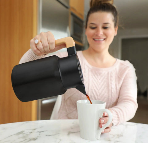 Woman pouring coffee from 50 Oz Stainless Steel Thermal Coffee Carafe Insulated Vacuum Double Walled Beverage Dispenser into mug.