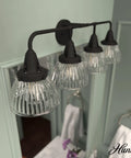 Cypress Grove 4 Light Natural Black Iron Vanity Light With Clear Holophane Glass Shade, mounted above a bathroom mirror.