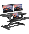 Sanodesk 35 Inch Electric Height Adjustable Standing Desk Converter Riser with dual monitors and laptop on black ergonomic surface.