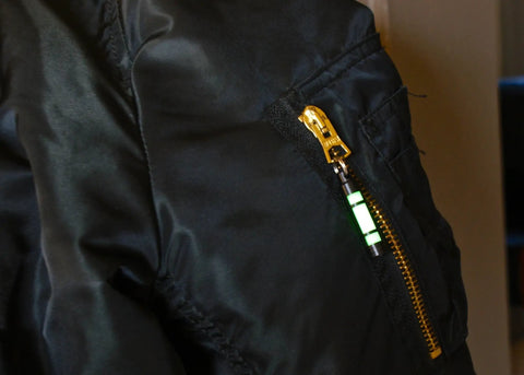 Embrite Glow Fob With Green Embrite Pellet, Aircraft-Grade Aluminum Keychain on black jacket zipper