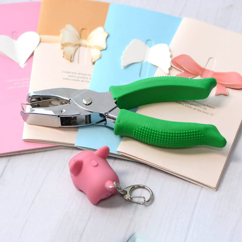 Two Pack Grab-and-Go Handheld Circle Hole Puncher Set 1/4 And 1/8 Inch, green handle, silver finish, on craft paper with pig keychain.