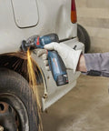 Compact 12 Volt Max Brushless Right Angle Die Grinder With Variable Speed Trigger grinding a car tire, producing sparks in a workshop.