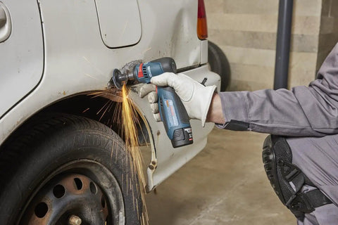 Compact 12 Volt Max Brushless Right Angle Die Grinder With Variable Speed Trigger grinding a car tire, producing sparks in a workshop.