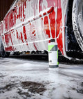 Red car covered in foam with Lift Pre Wash Snow Foam Car Wash Soap That Dissolves Dirt And Grime Like A Boss bottle underneath