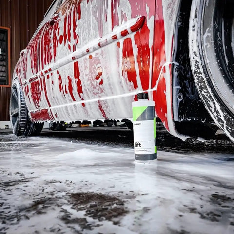 Red car covered in foam with Lift Pre Wash Snow Foam Car Wash Soap That Dissolves Dirt And Grime Like A Boss bottle underneath