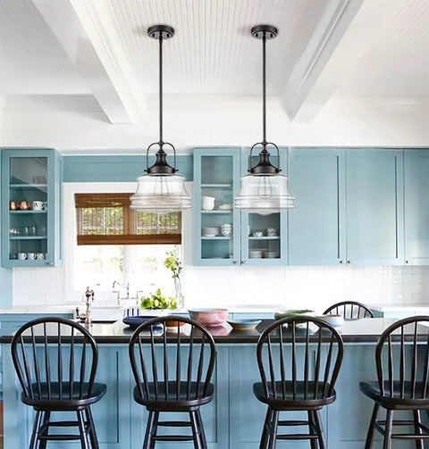 Black Farmhouse Pendant Light With Clear Glass Schoolhouse Style hanging over a kitchen island with blue cabinets and black chairs.