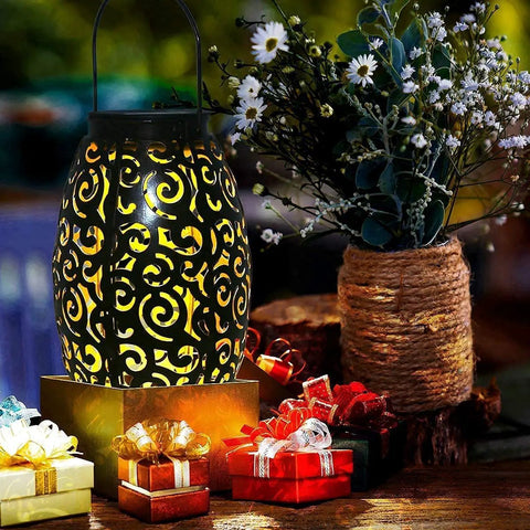 Solar Lantern Outdoor Hanging Light For Patio And Garden In Retro Metal Bronze Finish Waterproof Solar Garden Accent For Pathway And Yard Decor Easy Mount And Cozy Vibe Mother's Day Gift glowing next to flowers and gifts.