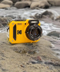 Rugged Waterproof Digital Camera With 50 Feet Depth Rating, 16MP Sensor, 4X Optical Zoom, placed on rocks by water