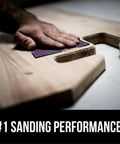 Hand using Pro Grade No Slip Grip Advanced Sandpaper 9 By 11 Inches 220 Grit Purple Clog Resistant for smooth wood surface finish.