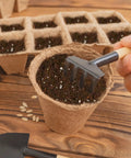 Hand holding a small rake over a pot filled with Seed Starting Soil Mix 1qt Ready To Use For Seedlings, ideal for vegetables and flowers.