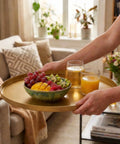 Round End Table With Removable Fabric Storage Basket And Tray Top held with drinks and fruit over a living room sofa.