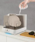 Portable Countertop Mini Dishwasher With 360 Degree Rotating Spray Heads And 1.59 Gallon Tank pouring water into appliance with clean plates visible.
