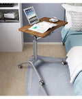 Adjustable Mobile Overbed Table Featuring Smooth Rollin Casters And Beastly Stable Base beside a bed with laptop and drink.