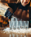 Bartender wearing black nitrile exam gloves, pouring liquid into tall glasses on ice, Black Nitrile Exam Gloves Medium 4 Mil Powder Free Latex Free Food Safe Medical Grade Puncture Resistant 100 Count Box Ideal For Medical And Food Handling And Laboratory Use Suitable For Medical Dental And Food Service Environments