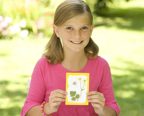 Child holding craft card made with Green Creativity Pressed Flower Art Kit With Recycled Flowers, for ages 5 and up.