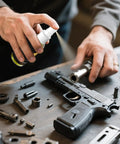 Person using All In One Gun Lube And Cleaner Kit with two oz and one oz needle oiler on disassembled firearm parts for maintenance