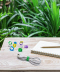 Super Handy Eighty Pack Of Eight Millimeter Numbered Leg Bands in vibrant colors on table with notebook and plants background
