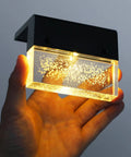 Hand holding a 3000K warm white color changing LED fixture, part of Solar Deck Lights 3000K Warm White Color Changing Outdoor Fence Lights For Steps Rails Walls Poolside LED Waterproof Patio Decor 6 Pack No Fuss Install Durable Weatherproof Solar Power, illuminated to show bubbles in the glass.