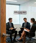 Conference room door with 'Employees Only' sign, showing two men and a woman in a meeting. Two Pack Employees Only Sign Stickers 9 By 2 And A Half Inches With Back Adhesive Metal Like Brushed Silver Finish Waterproof Fade Resistant Vinyl For Doors Walls Offices Stores Restrooms Keeps Unwanted Folks Out. on glass door.