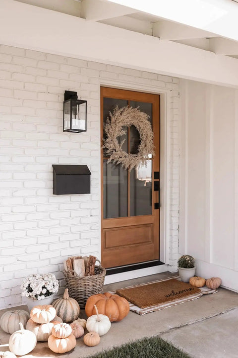 Outdoor Black Wall Sconce Light Fixture With Sturdy Iron Frame And Clear Glass Shade next to wooden front door with autumn decor
