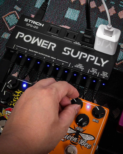 Hand adjusting knob on pedalboard with Ten Independent DC Outputs Guitar Pedal Power Supply For Effects visible.