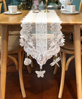 Lace table runner with butterfly and dragonfly tablecloth weights, on a wooden dining table set for tea.