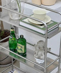 Slick Rolling Kitchen Island Trolley With Ample Storage Shelves And Quiet Locking Wheels For Mobile Coffee Bar Station Or Heavy Duty Stainless Steel Tool Caddy Rig with shelves holding drinks and decorative items.