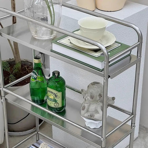 Slick Rolling Kitchen Island Trolley With Ample Storage Shelves And Quiet Locking Wheels For Mobile Coffee Bar Station Or Heavy Duty Stainless Steel Tool Caddy Rig with shelves holding drinks and decorative items.