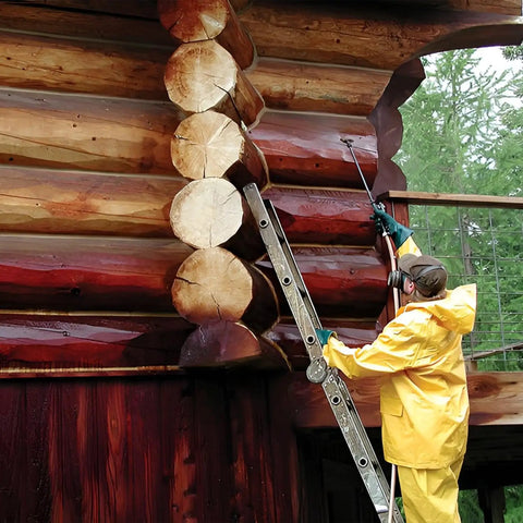 Person applying Top Shelf Log Home Stain And Sealer Combo In Semi Transparent Chestnut Tone with a brush on log cabin walls.