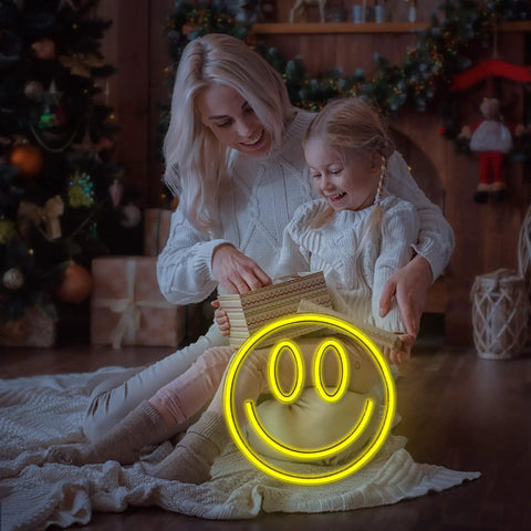 Happy Face Neon Sign LED Neon Light Wall Decor USB Powered Yellow Neon for Bedroom Kids Room Wedding Party Brighten Your Space With A Fun Modern Accent And Everyday Vibe placed near a mother and child opening gifts in a cozy room.