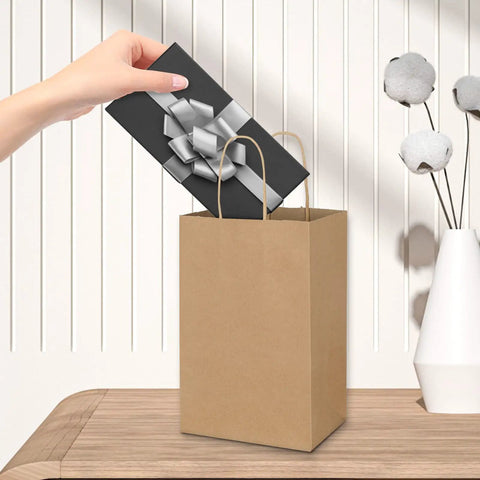 Hand placing gift into Bulk Brown Kraft Paper Bags With Handles 100 Pack Small Gift Bags 5.25 By 3.25 By 8.25 Inches Durable