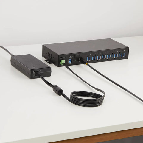 Built Like A Tank 16 Port Industrial USB 3.2 Gen 1 Hub With Heavy Duty Metal Casing and power supply cables on a table.