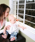 Mother and baby near window with Swing Open Style 6 Bar Window Guard For Child Safety White Finish Adjustable Width 24 To 42 Inches.