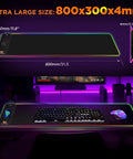 RGB Gaming Mouse Pad With 15W Wireless Charging Hella Large Non Slip Desk Pad For Gaming 10 Light Modes Premium Smooth Surface Oversized Mouse Mat For PC Office And Home Setup 31.5 By 11.8 Inches on a desk with keyboard and mouse.