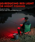 Person night fishing with bug-reducing red light illuminating the scene, sitting on a chair by a river, enhancing night vision.