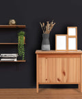 Wooden cabinet against black wall with decorative vase and frames, floating shelf with trailing plant and books
