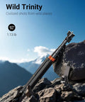 66 Inch Phone Tripod With Remote And Clamp Mount on rocky terrain, folded, aluminum build, with scenic mountain backdrop.