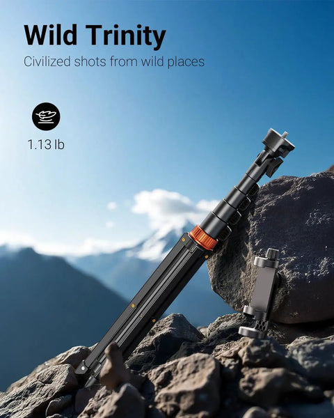 66 Inch Phone Tripod With Remote And Clamp Mount on rocky terrain, folded, aluminum build, with scenic mountain backdrop.