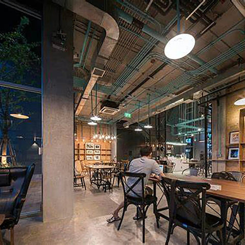 Modern industrial-style cafe interior with exposed pipes and varied seating.