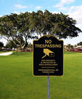 No trespassing sign in a park with tree background, text warns about video surveillance and prosecution.