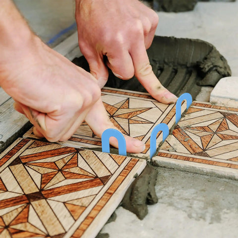 Hands installing tiles with tile leveling system spacers 1 16th inch horseshoe shims U shape clips for marble porcelain ceramic tiles.